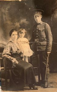 Man in uniform, with a seated woman and small child.